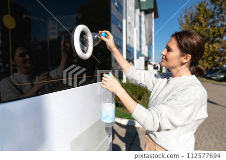 Woman uses a self service machine to receive used plastic bottles and cans on a city street.. 112577694