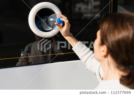 Woman uses a self service machine to receive used plastic bottles and cans on a city street.. 112577699