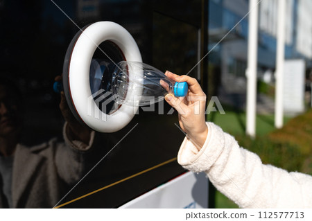 Woman uses a self service machine to receive used plastic bottles and cans on a city street.. 112577713