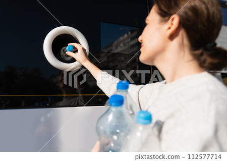 Woman uses a self service machine to receive used plastic bottles and cans on a city street.. 112577714