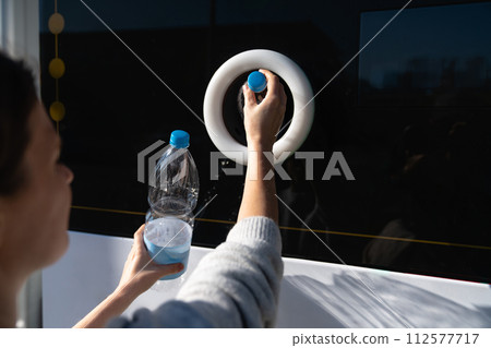 Woman uses a self service machine to receive used plastic bottles and cans on a city street.. 112577717