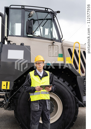 Engineer with tablet computer stands on the stairs to the cab of a truck. 112577936