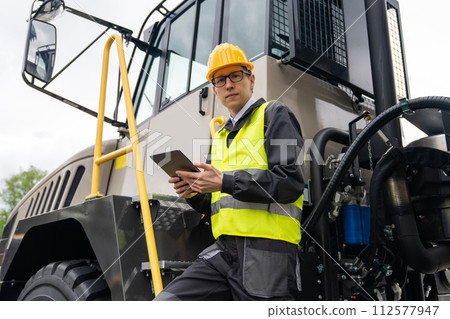 Engineer with tablet computer stands on the stairs to the cab of a truck. 112577947