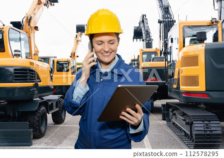 Engineer in a helmet with a digital tablet stands next to construction excavators 112578295