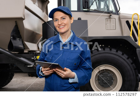 Woman worker with tablet computer stands next to mining truck 112578297