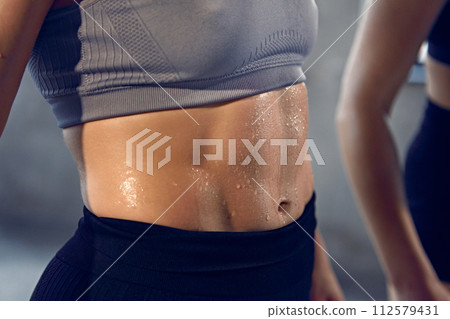 Close up of young woman with athletic body in sportswear wet after productive weightlifting training at gym. Close up of young woman with athletic body in sportswear wet after productive weightlifting training at gym. 112579431