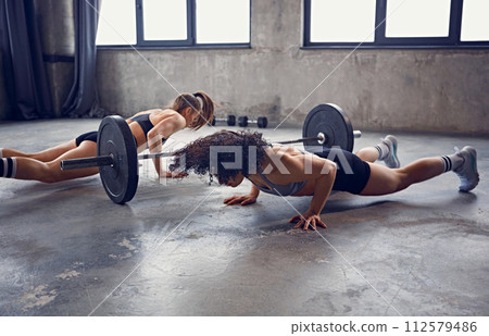 Dynamic portrait of young athlete women warming up doing some push ups in motion near barbell at gym. 112579486