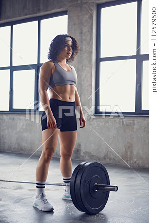 Full-length portrait of young athletic woman dressed sportswear stands preparing to lifting training with barbell. Ad Full-length portrait of young athletic woman dressed sportswear stands preparing to lifting training with barbell. Ad 112579500