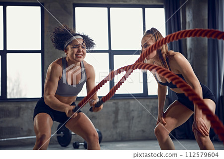 Strength training. Dynamic portrait of strong women athletes exercising in motion with battle ropes. Strength training. Dynamic portrait of strong women athletes exercising in motion with battle ropes. 112579604