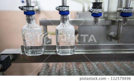 A row of glass bottles on a conveyor belt for the production of alcoholic beverages. 112579896