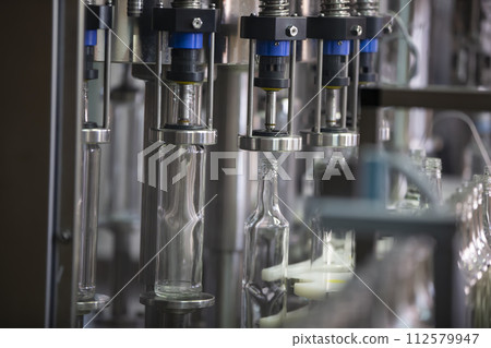 A long row of glass bottles on a conveyor belt. Production of alcoholic beverages. 112579947