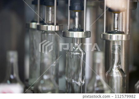 A row of glass bottles on a conveyor belt for the production of alcoholic beverages. A row of glass bottles on a conveyor belt for the production of alcoholic beverages. 112579982