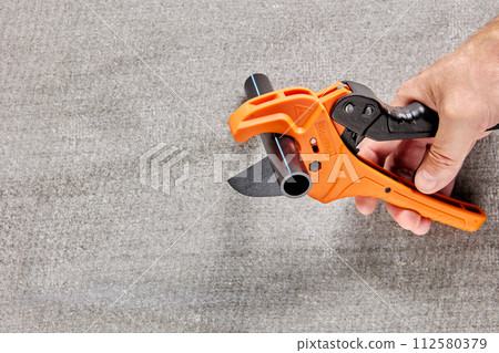 Plumber cuts piece from plastic pipe using ratchet pipe cutter. 112580379