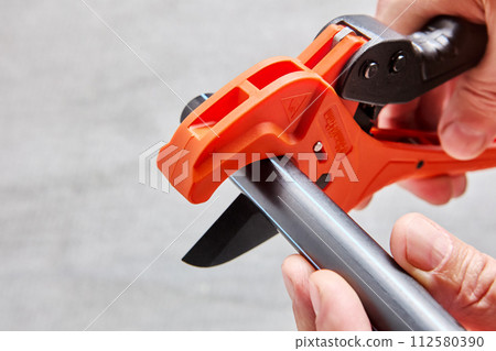 Plumber cuts end of plastic pipe with cutter. Plumber cuts end of plastic pipe with cutter. 112580390