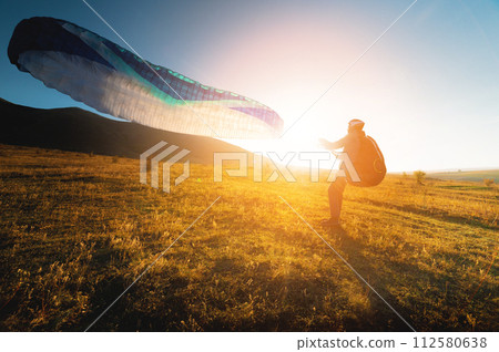 paraglider with a blue parachute takes off. A male athlete stands on the field and lifts a paraglider into the air 112580638