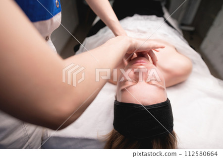 Cosmetic facial massage procedure. Close-up of the face of a young woman lying on her back, doing a face lifting massage, pinching and rolling technique Cosmetic facial massage procedure. Close-up of the face of a young woman lying on her back, doing a face lifting massage, pinching and rolling technique 112580664