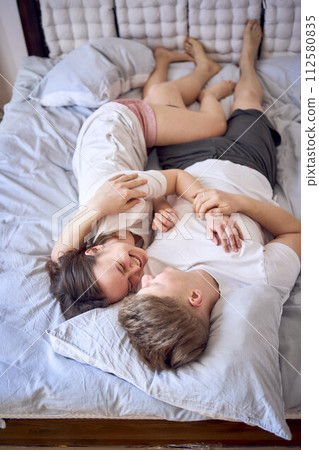 a young couple is lying on the bed, the girl is on the boy's shoulder, tender hugs 112580835