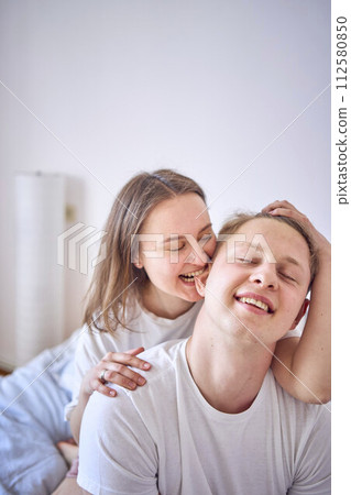 a young couple on the bed, the woman plays and bites the boy's ear 112580850