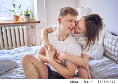 young couple on bed, woman hugs man from behind 112580853
