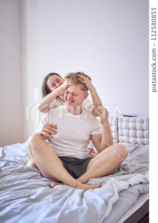 young couple on the bed, the woman combs the man's hair young couple on the bed, the woman combs the man's hair 112580855