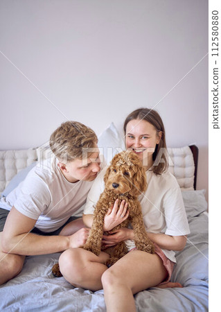 young couple is holding a cockapoo dog in their arms on the bed young couple is holding a cockapoo dog in their arms on the bed 112580880
