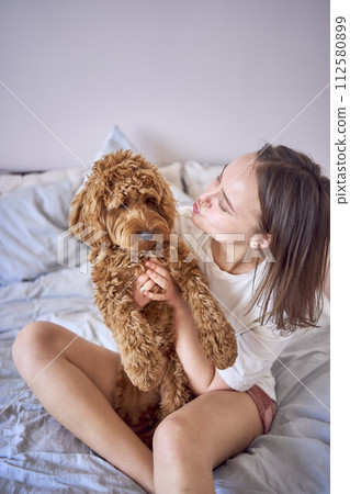 young woman playing and kissing cockapoo girl on bed, minimalism 112580899