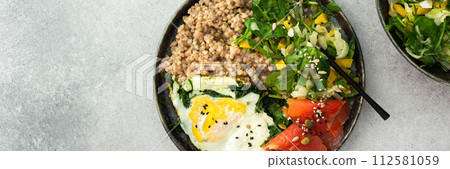 Buckwheat with fried egg and salmon fish, mix salad with fresh herbs and peppers 112581059