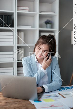 Happy Asian business women have the joy of talking on the smartphone, tablet, and laptop in the home office, Wearing a blue suite. 112581167