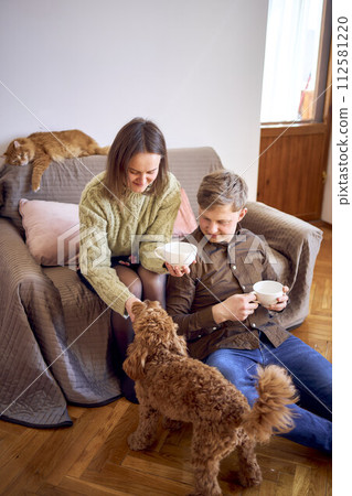 couple drinking from cups near sofa in living room, red cat sleeping on sofa, cockapoo running around 112581220