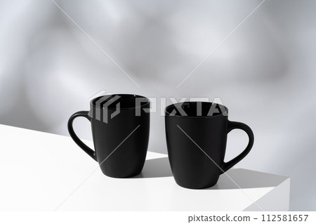 Two black ceramic mugs on gray background with shadows 112581657