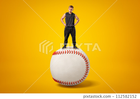 Strong muscular young man standing on big white baseball ball on yellow background 112582152