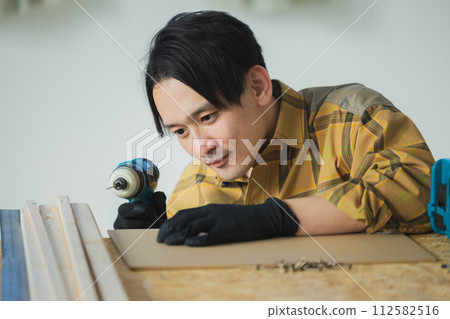 一個年輕人用電動螺絲起子工作 一個年輕人用電動螺絲起子工作 112582516