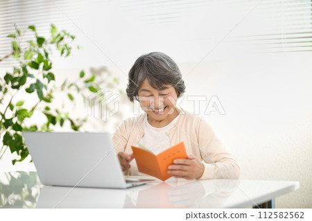 一位老年婦女一邊使用電腦，一邊查看她的退休金筆記型電腦 — 生命的終結 112582562