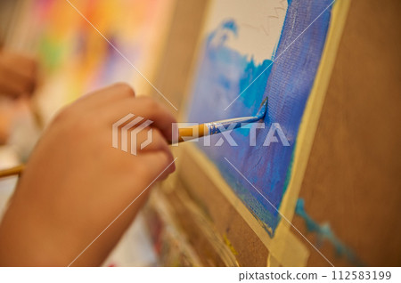 Close-up hand of a student holding paintbrush and painting picture on canvas in the art school. Close-up hand of a student holding paintbrush and painting picture on canvas in the art school. 112583199