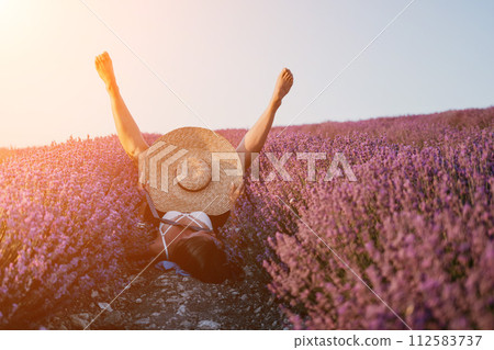 Woman lavender field. Happy carefree Woman legs stick out of the lavender bushes, warm sunset light. Bushes of lavender purple in blossom, aromatic flowers at lavender fields. 112583737