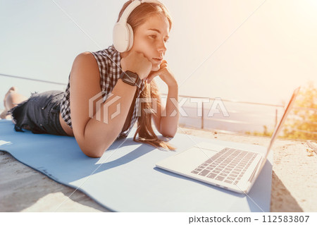 Woman laptop sea. Working remotely on seashore. Happy successful woman female freelancer working on laptop by the sea at sunset, makes a business transaction online. Freelance, remote work on vacation 112583807