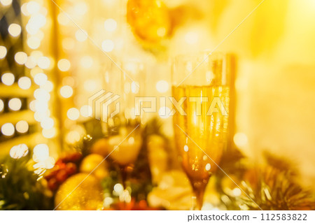 Two champagne glasses filled with champagne are placed on a table with a fruit arrangement. The glasses are surrounded by lights, creating a festive atmosphere. 112583822