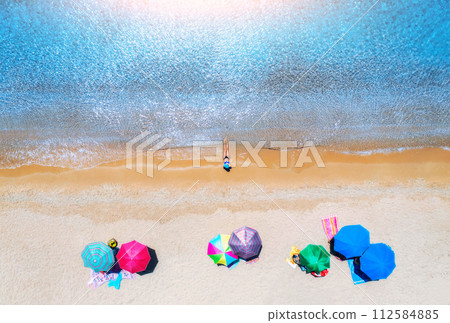 Aerial view of a woman on sandy beach, umbrellas and blue sea Aerial view of a woman on sandy beach, umbrellas and blue sea 112584885