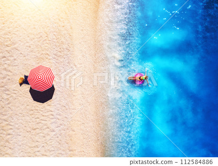 Aerial view of a woman in the sea, sandy beach and red umbrella 112584886