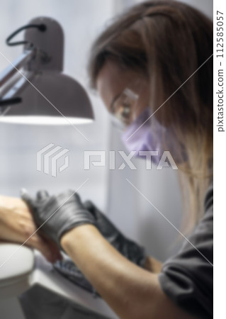 Manicurist at work. Professional manicurist removes old worn nail design from nails of client using modern electric drill. Blurred photo. Preparing fingernails for making fresh manicure 112585057