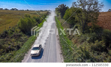 Looking down a gravel road with dust being blown by a vehicle. Path lined by power lines and trees Looking down a gravel road with dust being blown by a vehicle. Path lined by power lines and trees 112585330
