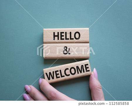 Hello and Welcome symbol. Concept words Hello and Welcome on wooden blocks. Beautiful grey green background. Businessman hand. Business and Hello and Welcome concept. Copy space. 112585858