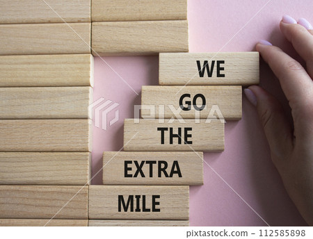 We go the extra mile symbol. Wooden blocks with words We go the extra mile. Beautiful pink background. Businessman hand. Business and We go the extra mile concept. Copy space. We go the extra mile symbol. Wooden blocks with words We go the extra mile. Beautiful pink background. Businessman hand. Business and We go the extra mile concept. Copy space. 112585898