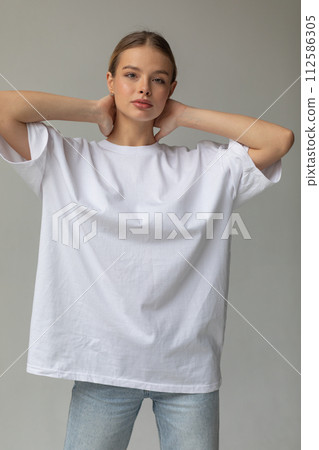 Beautiful blonde girl in a white oversized T-shirt and blue jeans posing on a gray background Beautiful blonde girl in a white oversized T-shirt and blue jeans posing on a gray background 112586305