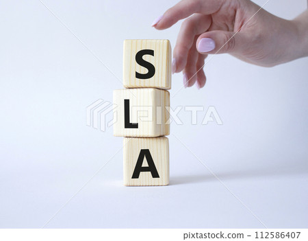 SLA - Service Level Agreement. Wooden cubes with word SLA. Businessman hand. Beautiful white background. Business and Service Level Agreement concept. Copy space. 112586407