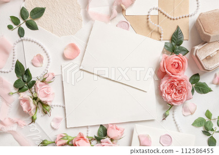 Blank cards near pink roses, engagement ring and silk ribbons top view, wedding mockup Blank cards near pink roses, engagement ring and silk ribbons top view, wedding mockup 112586455