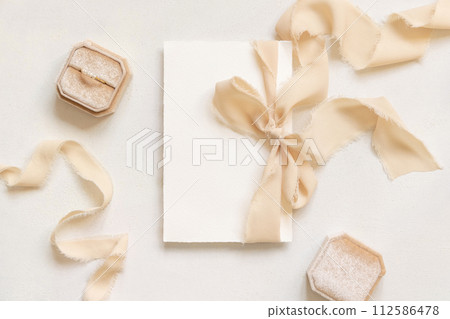 Card tied with a beige silk ribbons near engagement ring on white table top view, mockup Card tied with a beige silk ribbons near engagement ring on white table top view, mockup 112586478