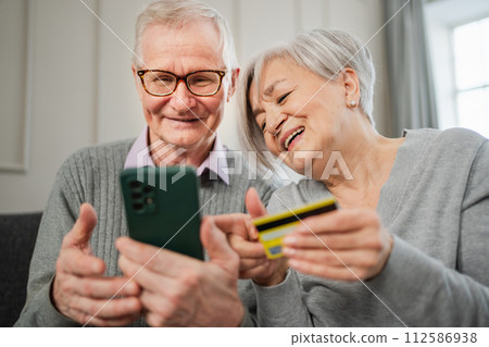 Senior couple man woman shopping online with smartphone paying with credit card. Old people buying on Internet enter credit card details at home indoors. Online shopping delivery service ecommerce 112586938