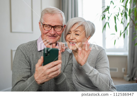 Video call. Happy senior couple woman man with smartphone having video call. Mature old grandmother grandfather talking speaking online. Older generation modern tech usage. Virtual meeting online chat 112586947