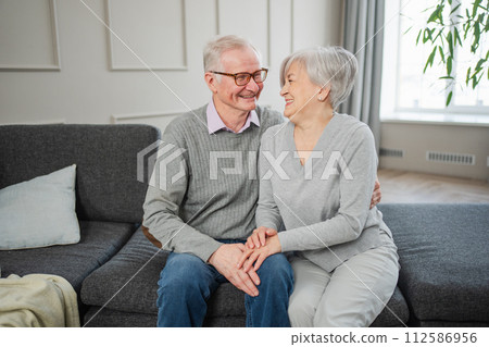 Senior adult mature couple hugging at home. Mid age old husband and wife embracing with tenderness love enjoying sweet bonding wellbeing. Grandmother grandfather together. Family moment love and care 112586956